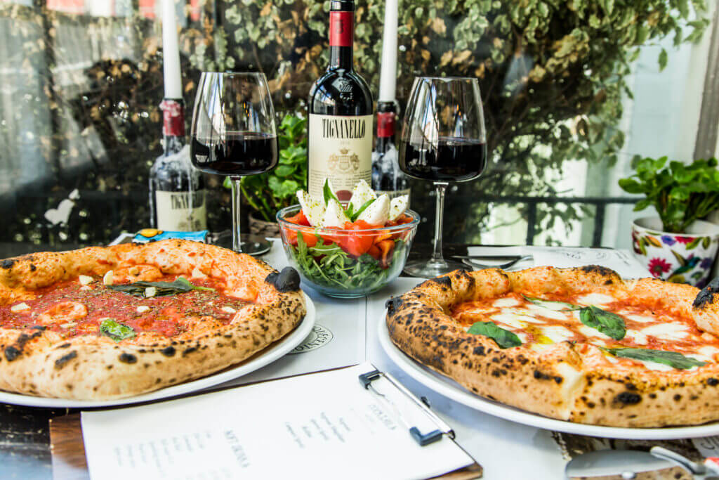neapolitan pizzas on table with glass of wine